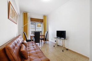 A living room with a brown leather sofa, a dining table with chairs, a TV on a stand, and a window with curtains. - Apartment 'Happy House Central' with Private Terrace, Balcony and Wi-Fi (Faro)