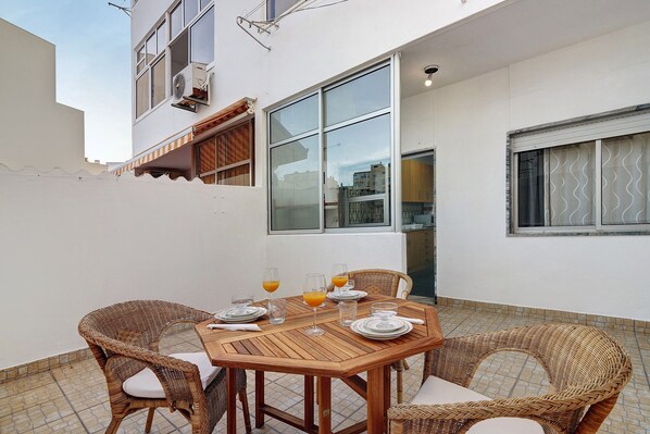 A dining area with a wooden table and wicker chairs, a window with a view, and a balcony with a tiled floor. - Apartment 'Happy House Central' with Private Terrace, Balcony and Wi-Fi (Faro)
