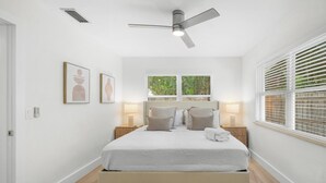 Ein modernes Schlafzimmer mit Bett, Nachttischlampen, Deckenventilator und einem Fenster mit Jalousien.