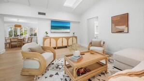 Ein geräumiges Wohnzimmer mit hohen Decken, einem Essbereich mit Tageslicht und Blick auf den Strand durch die Fenster.