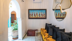 A room with a patterned floor, a sofa with cushions, a hanging light fixture, a framed painting, and a wall-mounted mirror. - Riad Nejma BenYoussef (Marrakech)