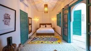 A bedroom with a bed, a patterned rug, and green doors. - Riad Nejma BenYoussef (Marrakech)