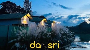 A serene lakeside view at dusk with two illuminated structures, possibly a gazebo or pavilion, surrounded by lush vegetation. - Daosri The Inn (Barangabari)