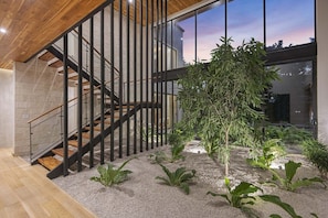 A modern interior with a staircase, indoor plants, and a view through large windows.