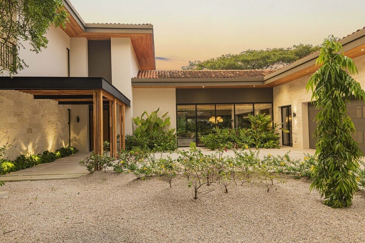 Une maison moderne avec une façade en pierre, une terrasse en bois et une cour intérieure recouverte de gravier.