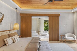 A modern bedroom with a large bed, a ceiling fan, and a view to an outdoor area.