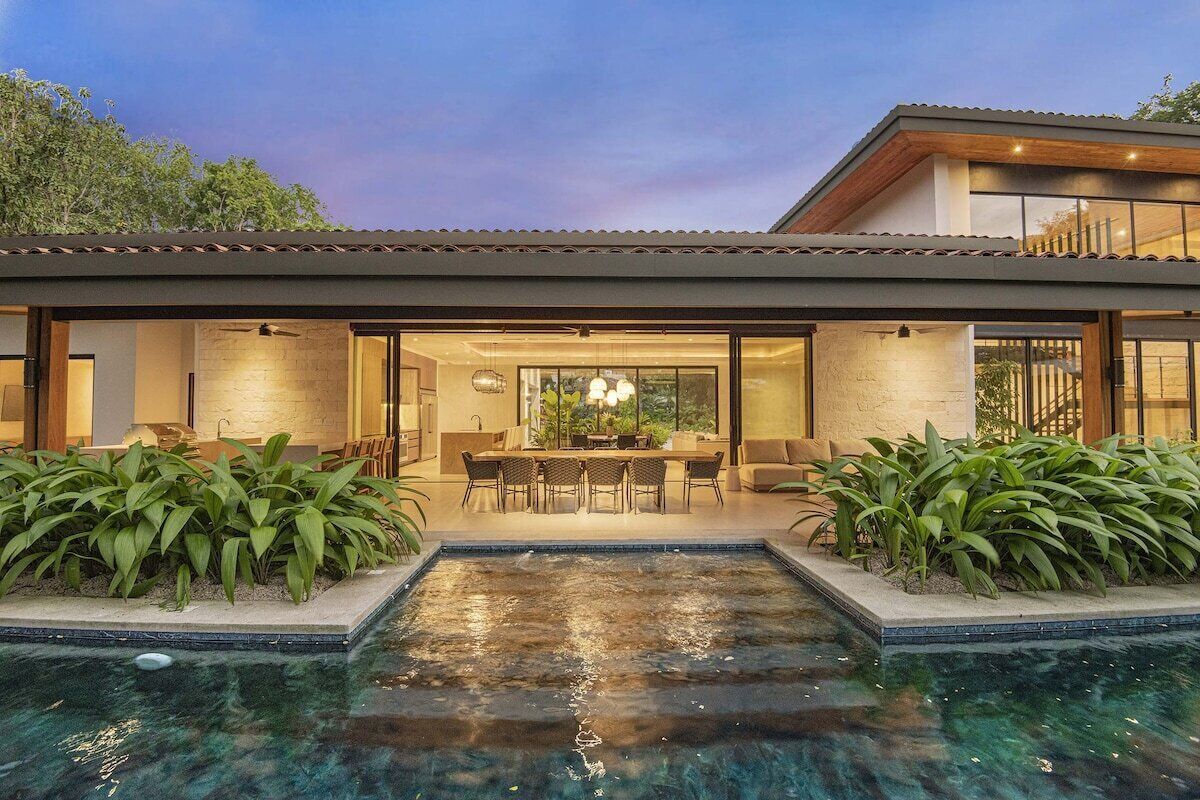 Una casa moderna amb una piscina, zona de menjador i una finestra gran que donen a la piscina.