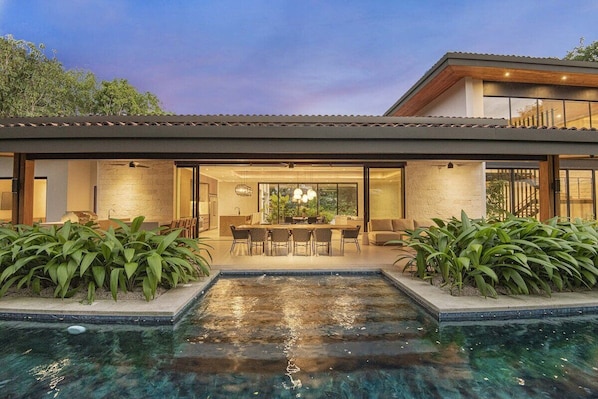 Una casa moderna con piscina, comedor y un amplio ventanal con vistas a la piscina.