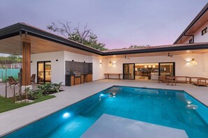 Ein moderner Poolbereich im Freien mit integrierter Küche und Sitzgelegenheit.