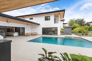 Ein modernes Haus mit Swimmingpool, überdachter Terrasse und Garten.