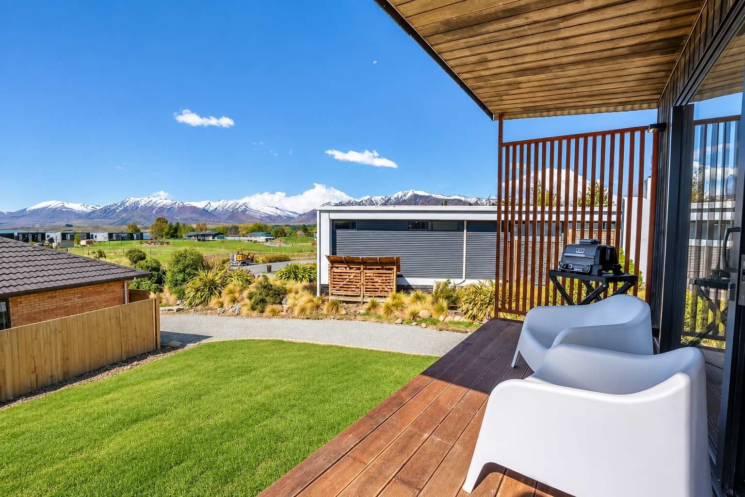 A modern outdoor patio with a wooden deck, a white chair, and a barbecue grill.
