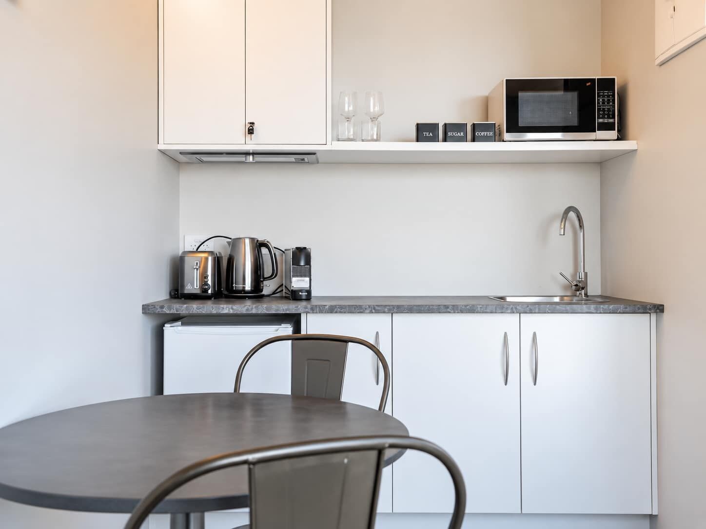 Een compacte keuken met witte kastjes, een magnetron, een koffiezetapparaat en een waterkoker.