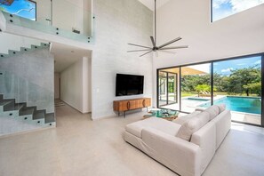 Ein modernes Wohnzimmer mit Flachbildfernseher, einer Couch und Blick auf einen Pool.
