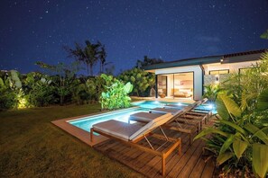A swimming pool with lounge chairs, surrounded by greenery, under a starry night sky. - Lingalonga (Guanacaste)