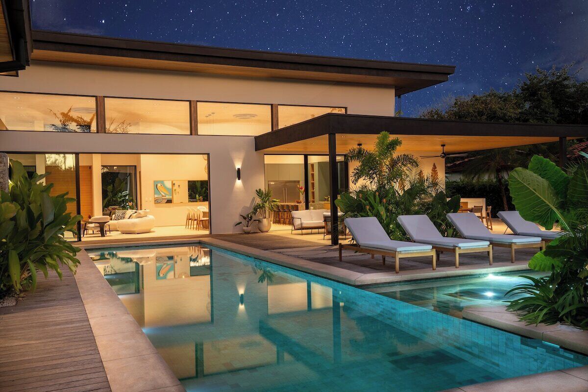 Een modern huis met een zwembad, lounge stoelen en een terras.