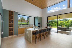 A modern kitchen with a large island, bar stools, and a view of a lush garden. - Lingalonga (Guanacaste)