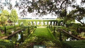 Un jardín formal con césped central, senderos simétricos y estructuras en arco.