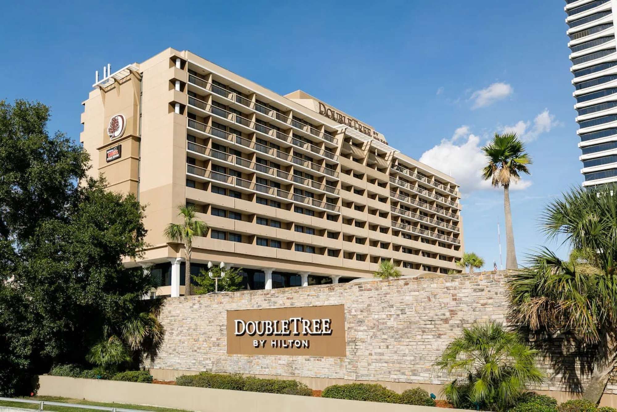 Een hotel met een beige gevel, meerdere balkons en een bord met de tekst 'DOUBLETREE BY HILTON'.