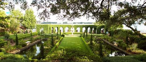 A formal garden with a central lawn, symmetrical pathways, and arched structures.