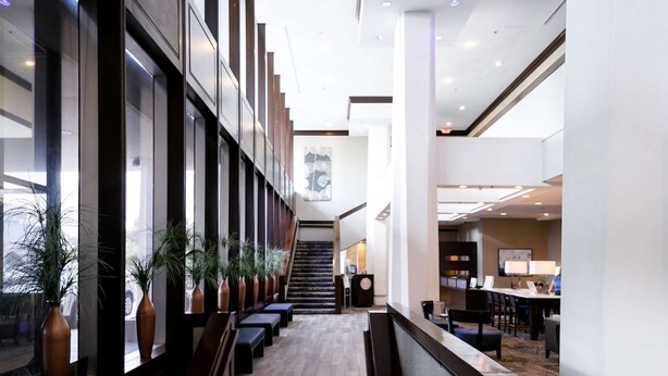 Un hall d’hôtel moderne avec un long comptoir d’accueil, plusieurs espaces aménagés pour s’asseoir et un escalier menant aux étages supérieurs.