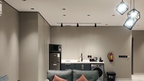 Un salon moderne avec un canapé gris, une table basse en bois et un coin cuisine à l’arrière-plan.