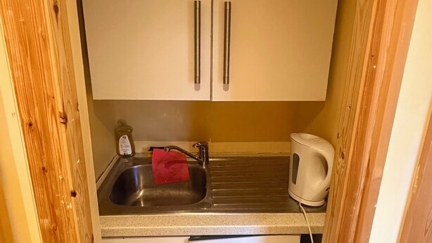 Ett kompakt kök med två vita skåp, en diskho i rostfritt stål och en vattenkokare på bänkskivan.