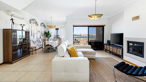 A modern living room with a sofa, TV, and dining area. - Casa Bayview Bliss - Sea Views, Pool & BBQ, Stroll to Beach and Ferragudo Village (Ferragudo)
