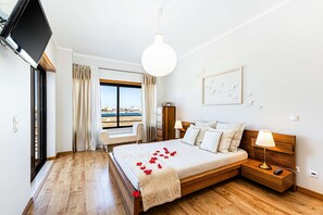 A bedroom with a bed, bedside table, lamp, and a view of the beach.