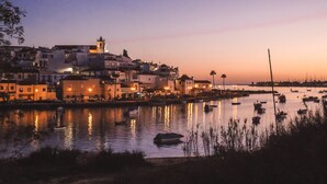 A coastal town at dusk with buildings along the waterfront and boats in the water. - Casa Bayview Bliss - Sea Views, Pool & BBQ, Stroll to Beach and Ferragudo Village (Ferragudo)
