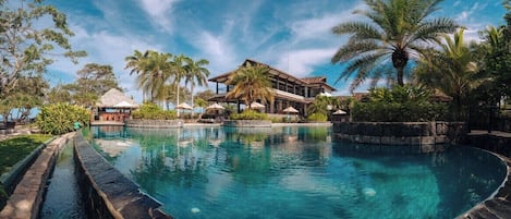 A resort with a swimming pool, palm trees, and a building with a thatched roof.