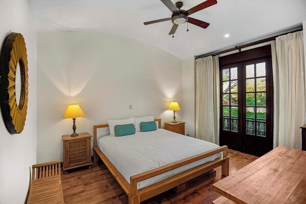 Un dormitorio con cama de madera, dos lámparas de noche, ventilador de techo y ventana con cortinas.