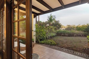 A view from a room with a large window opening to a garden area with a lawn and various plants. - Villa Mansita (Tamarindo)