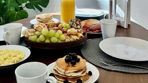Une table de petit-déjeuner avec divers aliments, une bouteille de jus d’orange et un luminaire moderne.