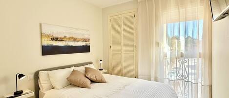 A bedroom with a bed, a nightstand, a lamp, a painting, and a balcony with a view.