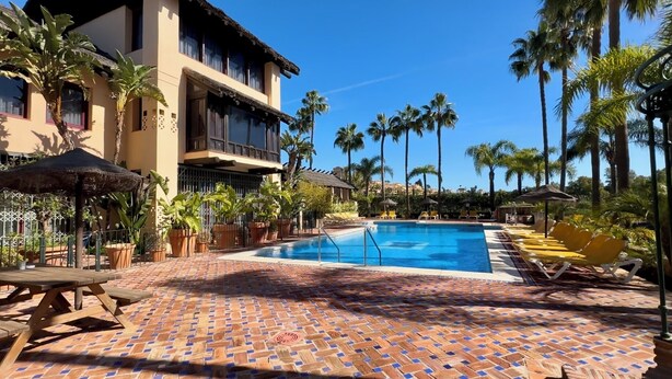 Un espace piscine doté d’une terrasse carrelée, de chaises longues et de palmiers.