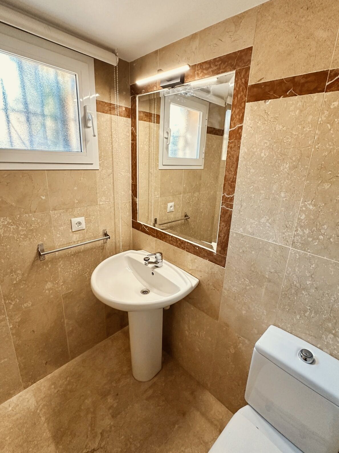 A bathroom with a pedestal sink, a mirror, and a toilet.