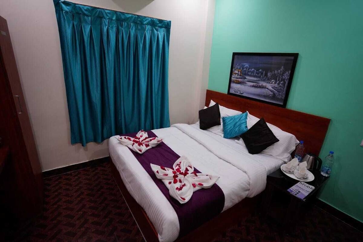 A hotel room with a bed, a nightstand, a framed picture on the wall, and a window with curtains.