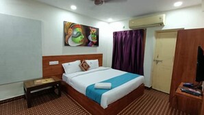 Quarto de hotel com cama, mesa de cabeceira, quadro na parede, porta e unidade de ar condicionado.