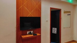 Quarto com televisão fixada numa divisória de madeira, uma porta com placa de 'Não Fumar' e um espelho na parede.