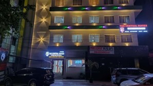 Um hotel com vários andares, janelas iluminadas e uma placa com a inscrição 'The Central Suites' indicando quartos disponíveis.