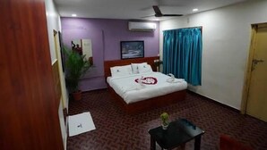 Quarto de hotel com cama, uma mesinha, um vaso de planta e um ventilador de teto.