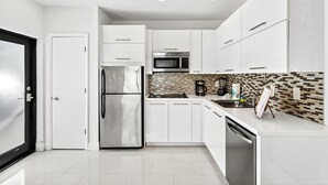 A modern kitchen with white cabinetry, stainless steel appliances, and a tiled backsplash. - Sleek Kitchenette & Queen Bed (Fort Lauderdale)