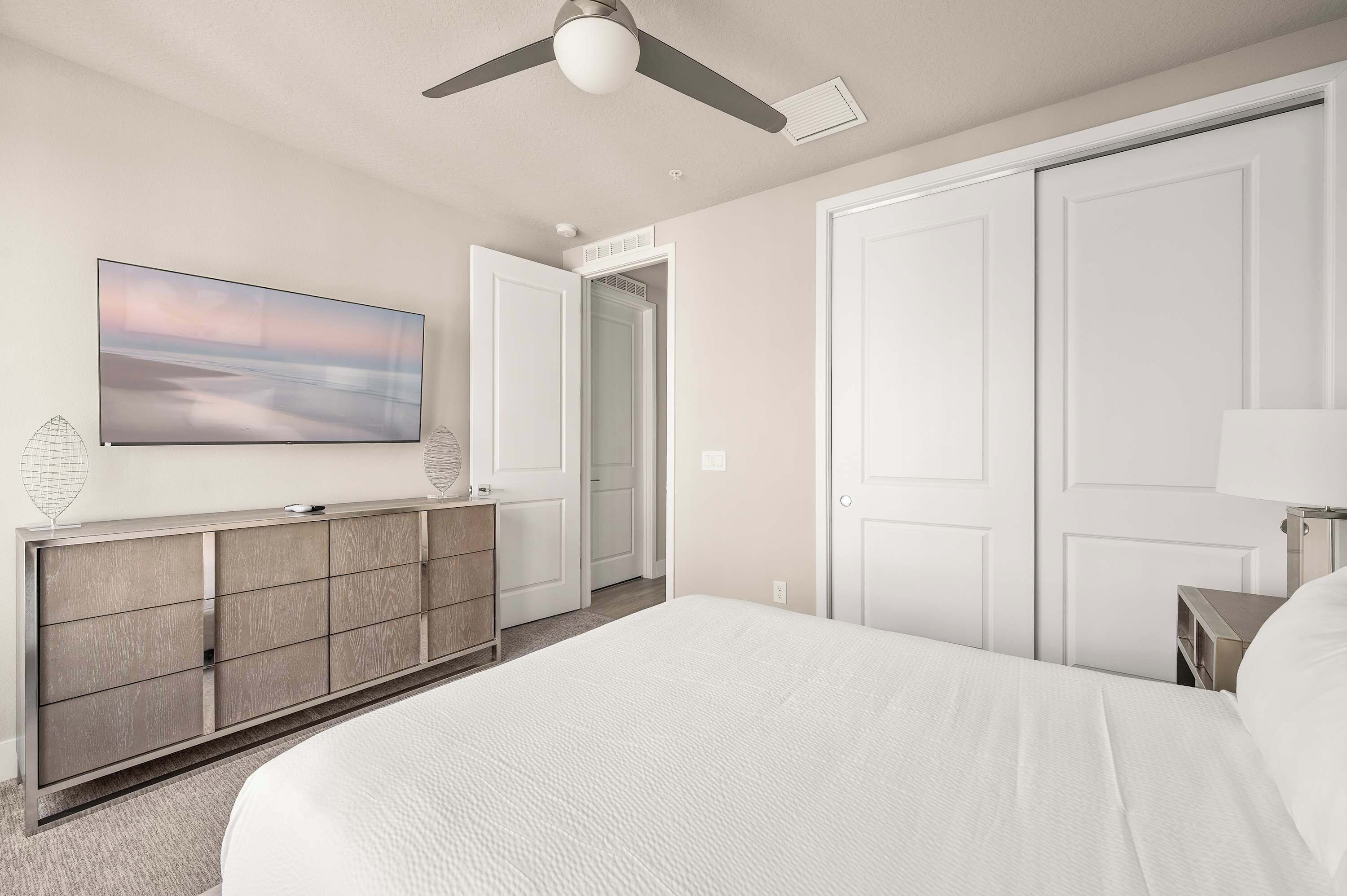 A bedroom with a large bed, a ceiling fan, a TV on a cabinet, and a door leading to a closet.