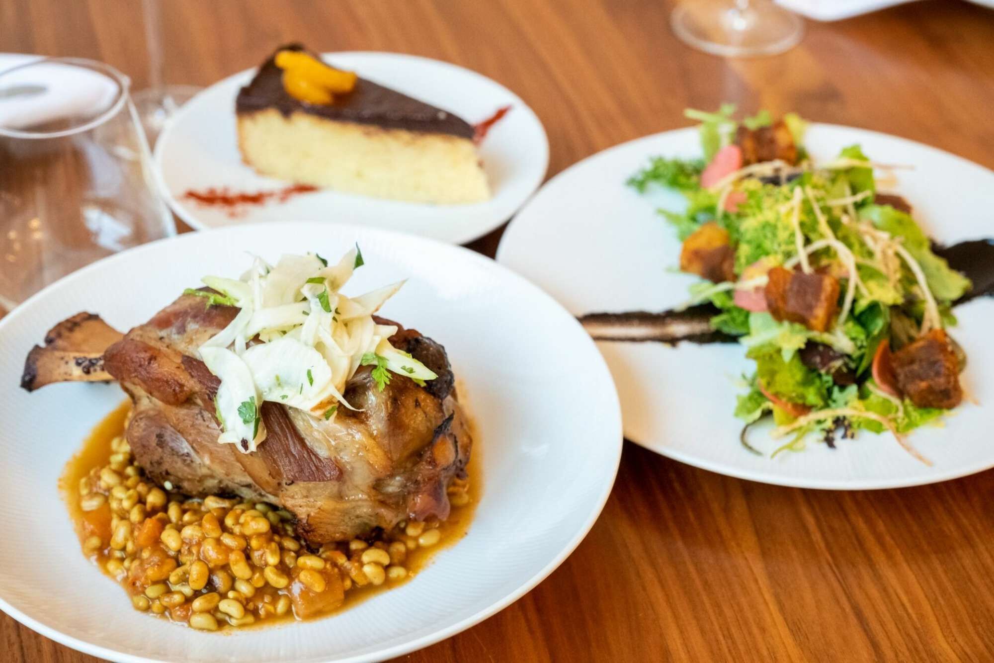 Un tavolo da pranzo con tre piatti di cibo: un piatto di carne e fagioli, una cheesecake e un'insalata.