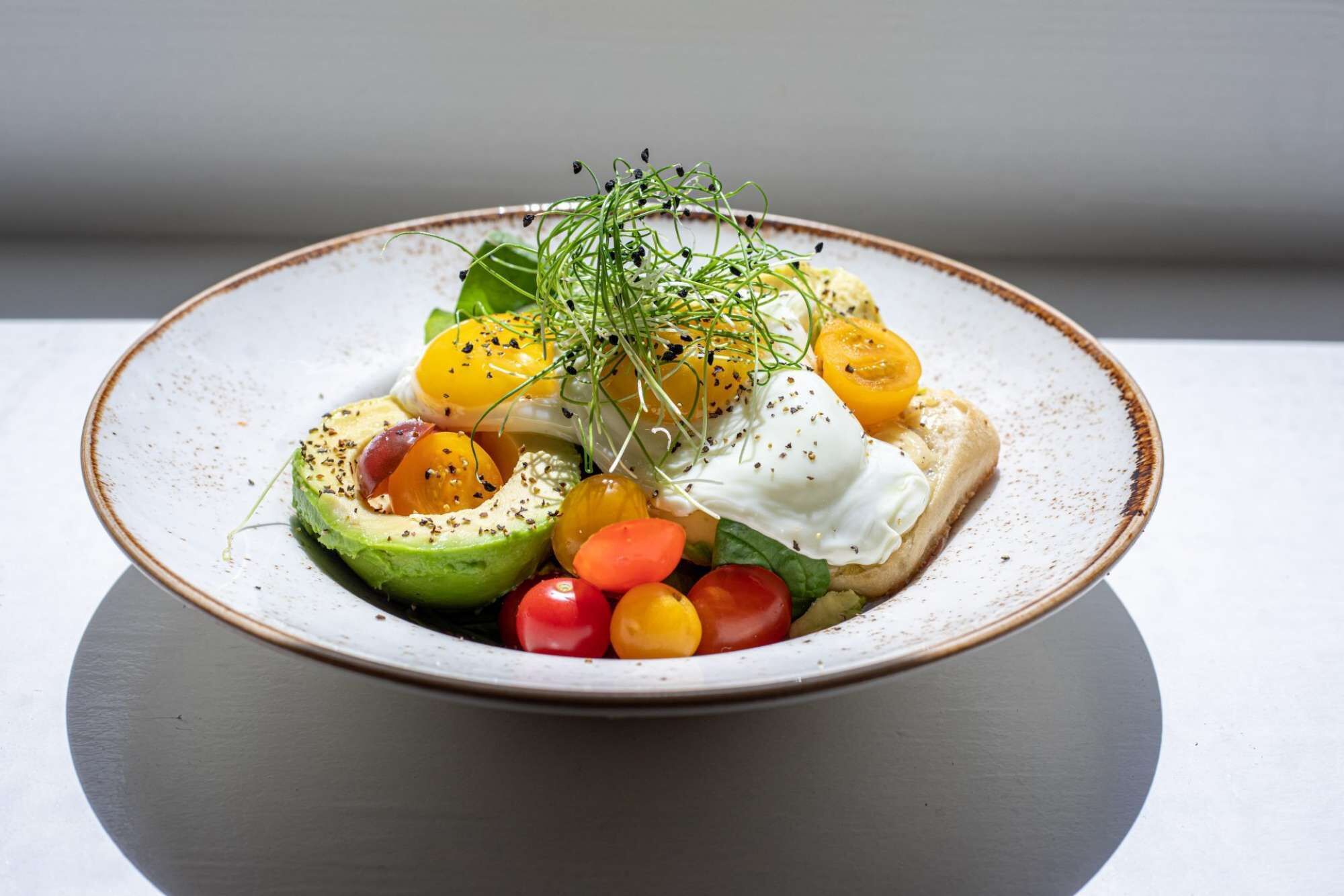 Ein Teller mit Essen, darunter Avocado, Tomaten und ein pochiertes Ei.
