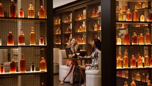 Un coin bar avec deux personnes assises à une table, entourées d’étagères remplies de bouteilles.
