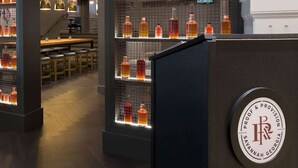 Un espace bar avec des étagères remplies de bouteilles d’alcool, un comptoir orné d’un logo et un coin salon avec des tables et des chaises.