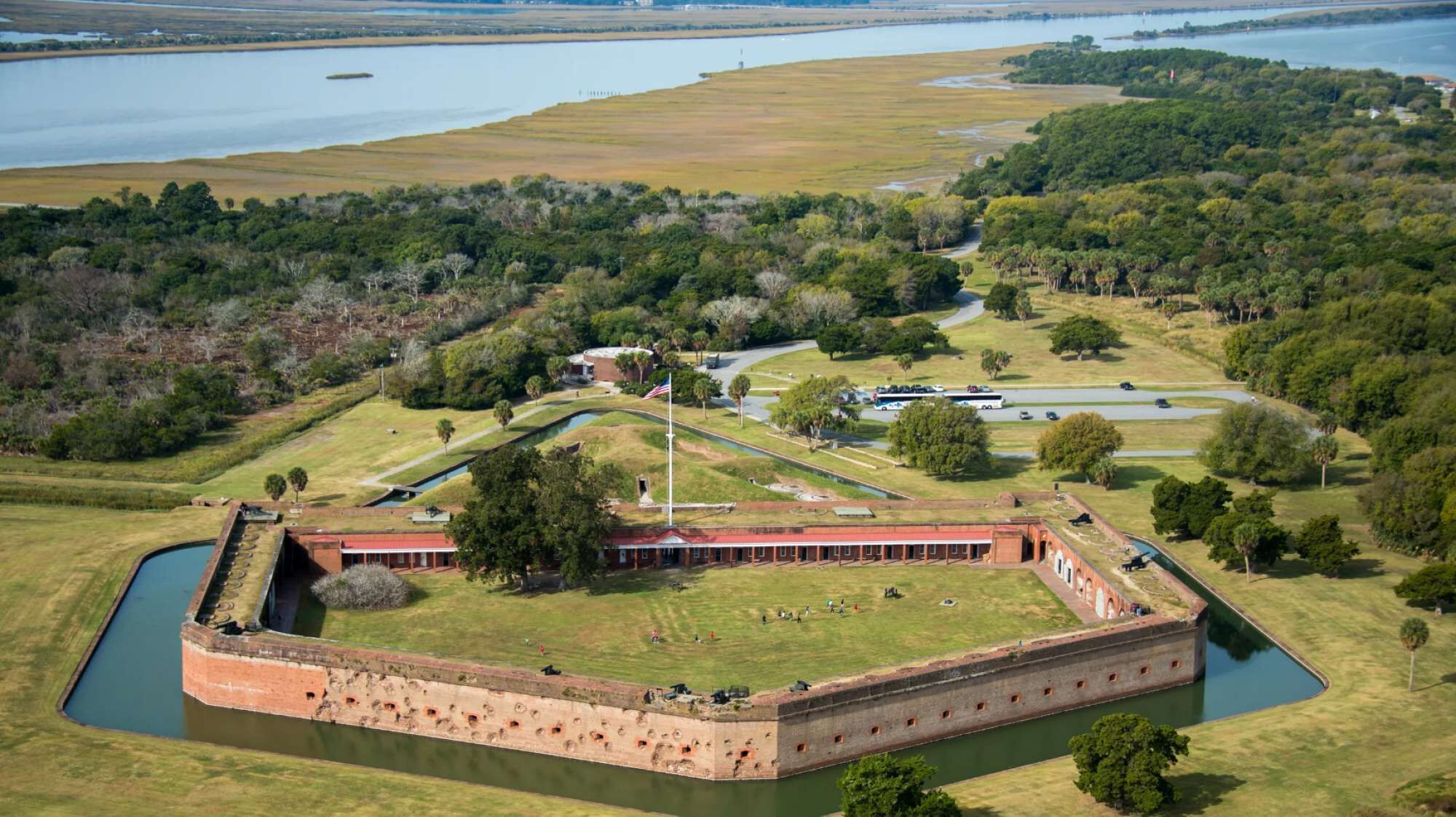 A large fort with a moat, surrounded by grassy fields and a body of water.