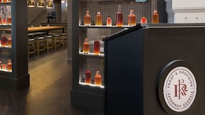 A bar area with shelves of liquor bottles, a counter with a logo, and a seating area with tables and chairs. - Walk to River Street | Pool. Dining + On-Site Bar (Savannah)