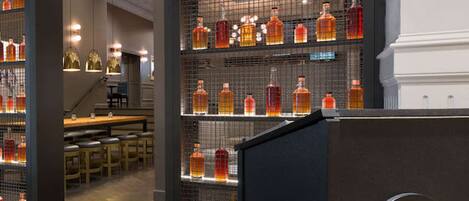 A bar area with shelves of liquor bottles, a counter with a logo, and a seating area with tables and chairs.